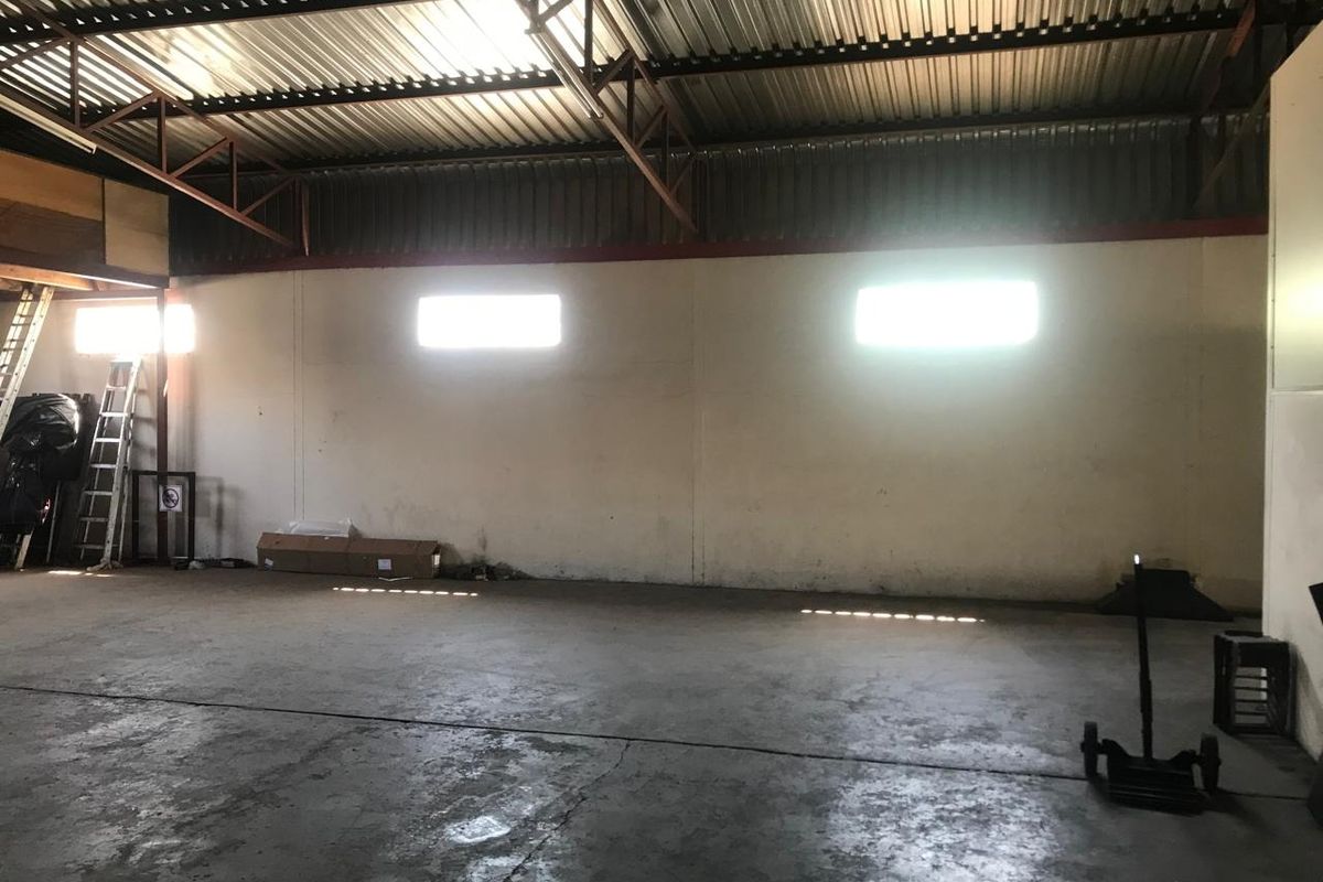 Spacious industrial utility area featuring high ceilings with exposed steel trusses, concrete flooring, and natural light from high-level windows.