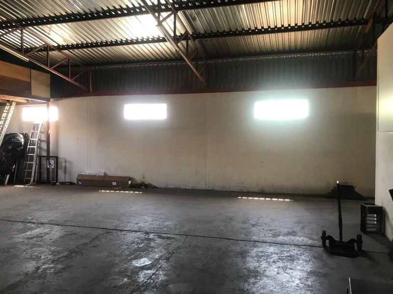 Spacious industrial utility area featuring high ceilings with exposed steel trusses, concrete flooring, and natural light from high-level windows.