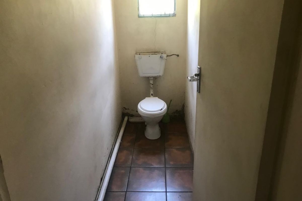 A small, dated bathroom featuring a standard toilet, tiled flooring, and a small window. The space requires significant cosmetic renovation and repairs.
