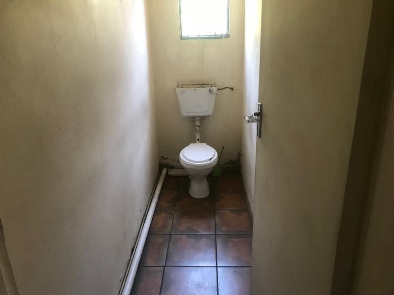 A small, dated bathroom featuring a standard toilet, tiled flooring, and a small window. The space requires significant cosmetic renovation and repairs.