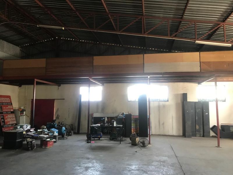 Spacious industrial utility area featuring high ceilings with exposed steel trusses, a mezzanine level, and durable concrete flooring, suitable for workshop or storage use.