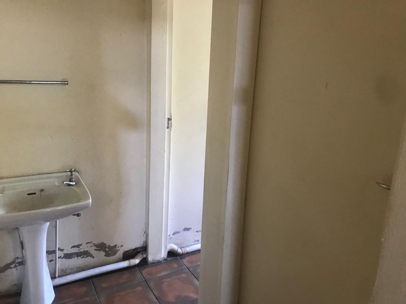 A small, dated bathroom area featuring a pedestal washbasin and tiled flooring, currently showing significant signs of wear and wall surface deterioration.