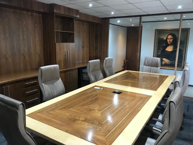 Professional boardroom featuring extensive built-in wooden cabinetry, a large central meeting table, suspended ceiling with recessed lighting, and a decorative mirrored wall feature.