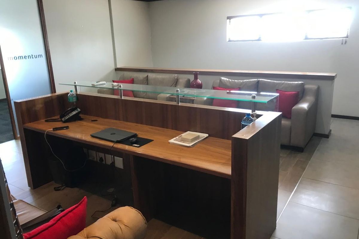 Professional office space featuring a custom built-in wooden desk with a glass partition, tiled flooring, and a modern suspended ceiling.