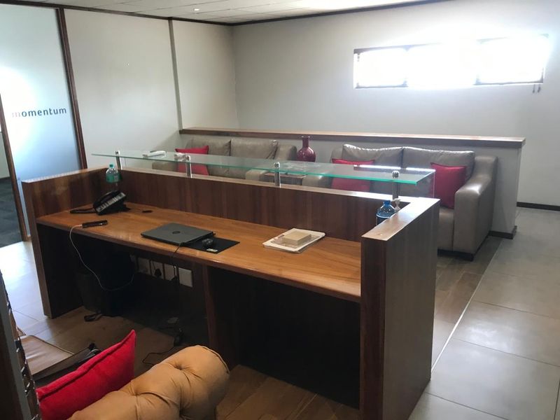 Professional office space featuring a custom built-in wooden desk with a glass partition, tiled flooring, and a modern suspended ceiling.