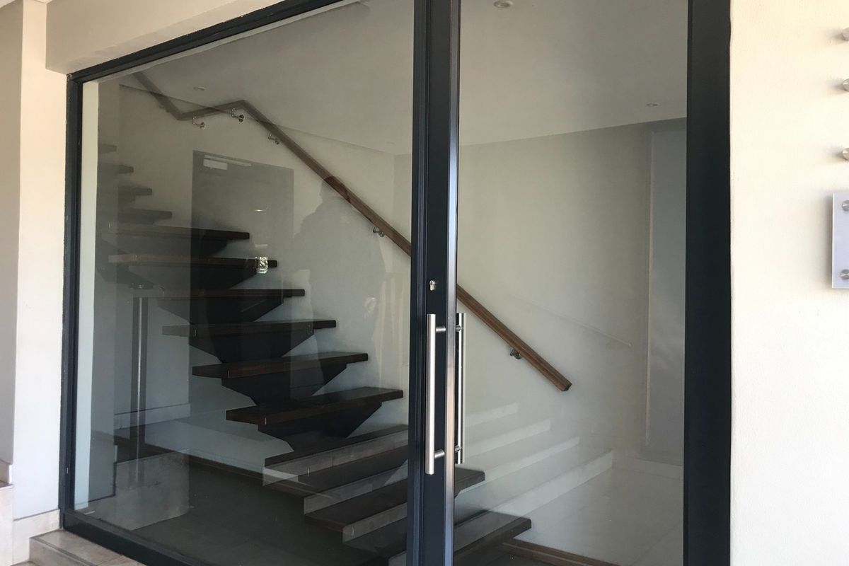 Modern office entrance featuring a glass door and a contemporary staircase with a wooden handrail.