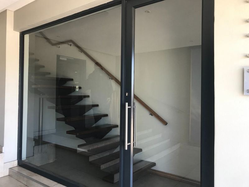 Modern office entrance featuring a glass door and a contemporary staircase with a wooden handrail.