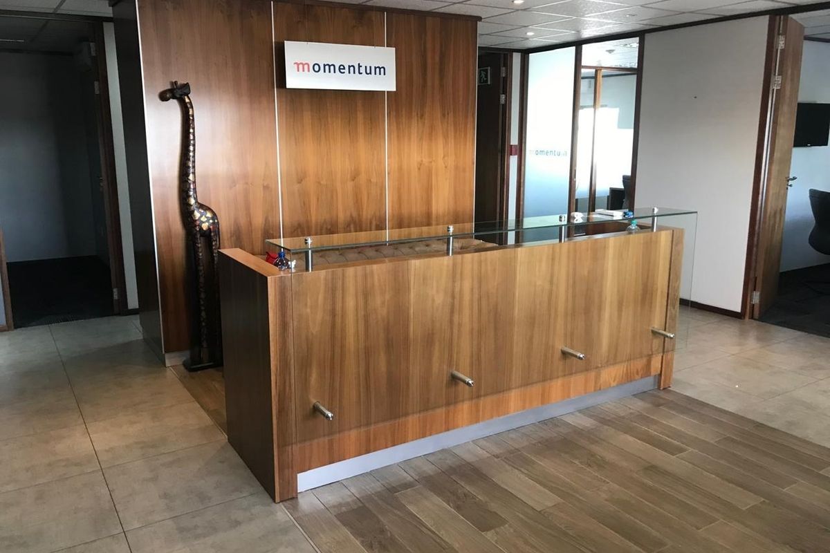 Professional office reception area featuring a modern wood-paneled reception desk, glass partitions, and clean tiled flooring.