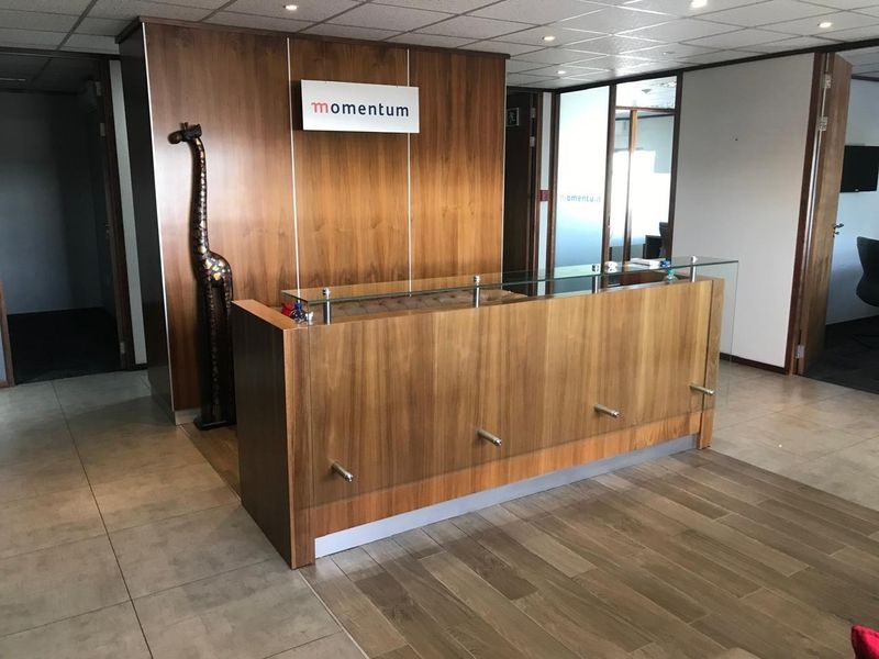 Professional office reception area featuring a modern wood-paneled reception desk, glass partitions, and clean tiled flooring.
