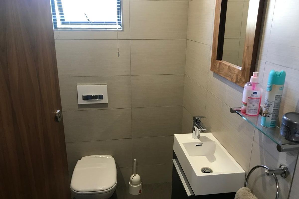 A compact modern bathroom featuring a wall-mounted toilet, a sleek vanity basin with a mixer tap, and neutral wall tiling.