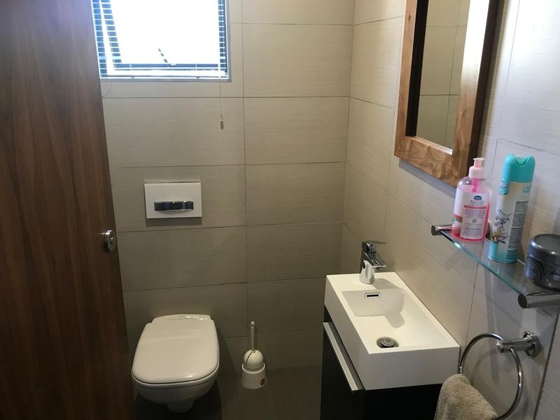 A compact modern bathroom featuring a wall-mounted toilet, a sleek vanity basin with a mixer tap, and neutral wall tiling.