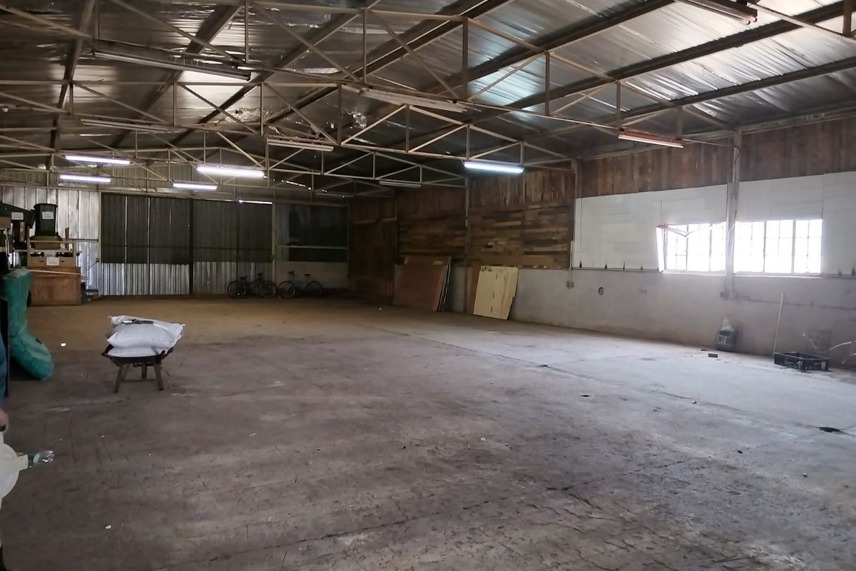 A large, open-plan industrial utility space featuring exposed steel roof trusses, concrete flooring, and corrugated metal wall cladding, suitable for storage or workshop use.