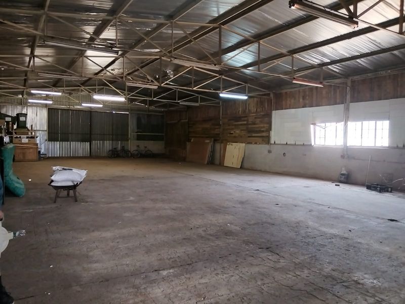 A large, open-plan industrial utility space featuring exposed steel roof trusses, concrete flooring, and corrugated metal wall cladding, suitable for storage or workshop use.