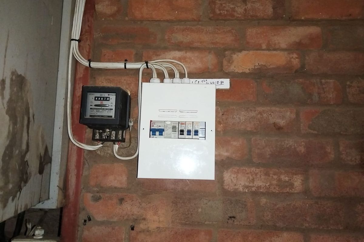 A utility area featuring a wall-mounted electrical distribution board and electricity meter installed on an exposed brick wall.