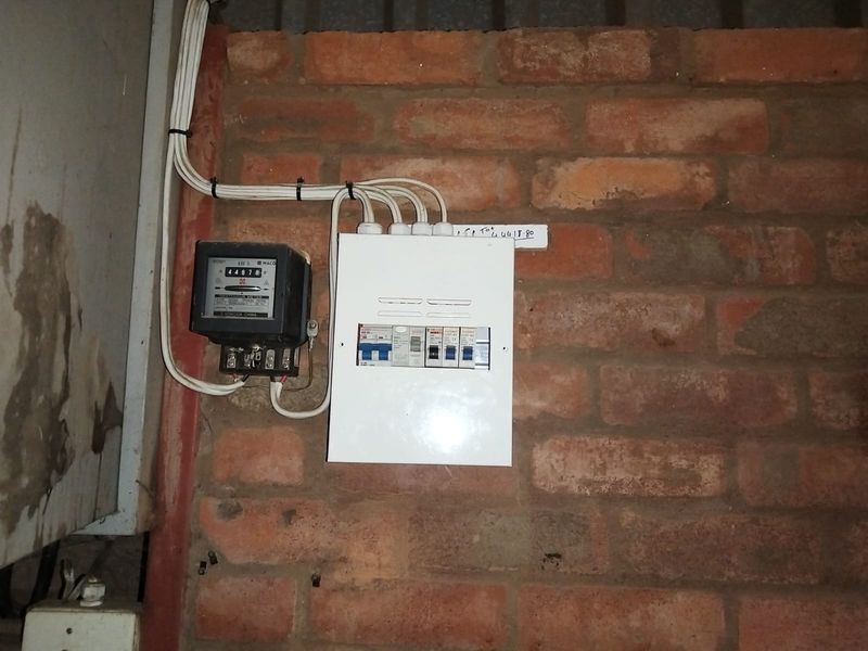 A utility area featuring a wall-mounted electrical distribution board and electricity meter installed on an exposed brick wall.