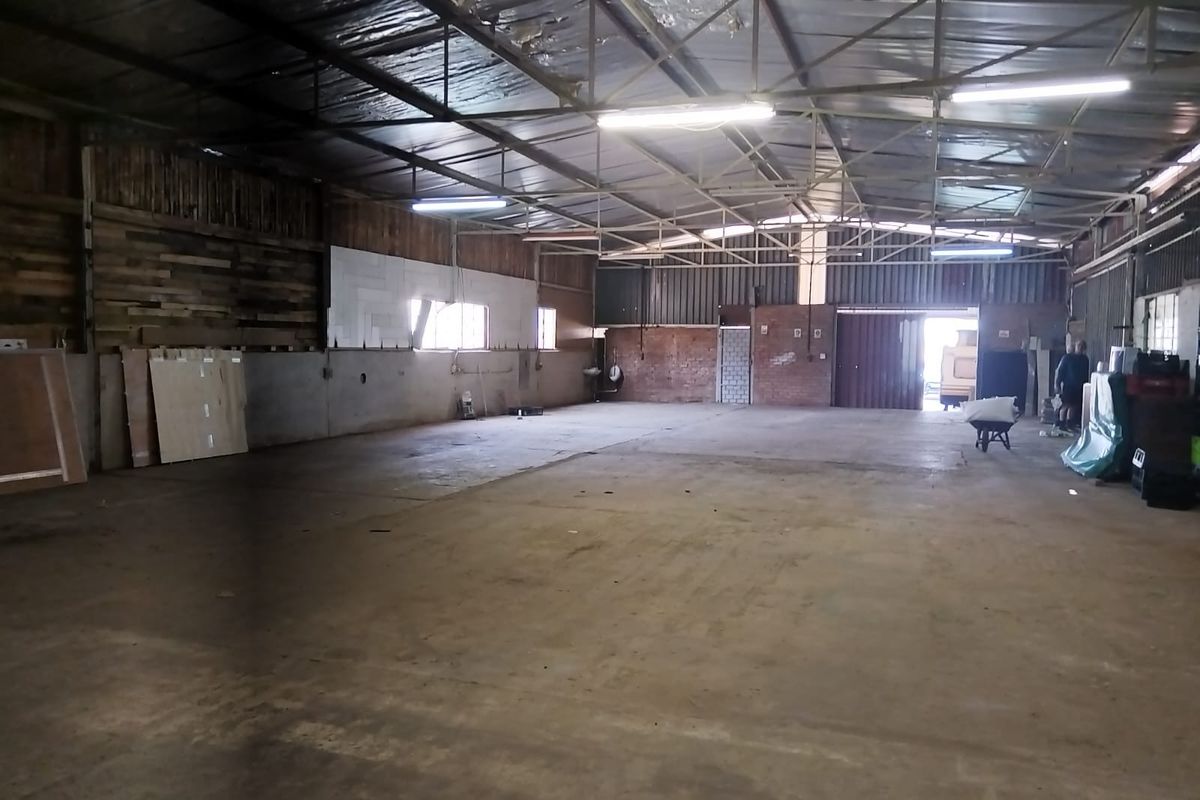 Spacious industrial warehouse featuring exposed steel roof trusses, concrete flooring, and a mix of brick and timber wall finishes with large roller door access.