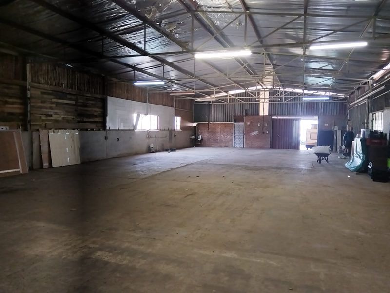 Spacious industrial warehouse featuring exposed steel roof trusses, concrete flooring, and a mix of brick and timber wall finishes with large roller door access.