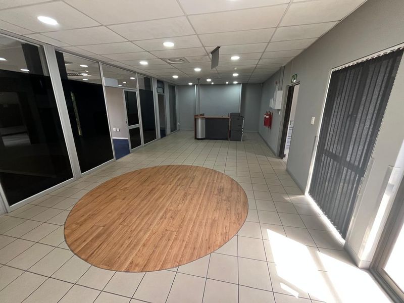 Spacious open-plan office area featuring ceramic tile flooring, glass partitioning, and recessed ceiling lighting, providing a clean and professional workspace environment.