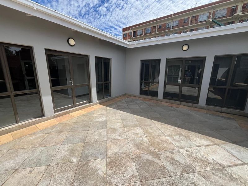 A clean, paved outdoor courtyard area featuring modern aluminium-framed glass doors providing access to the surrounding office spaces.