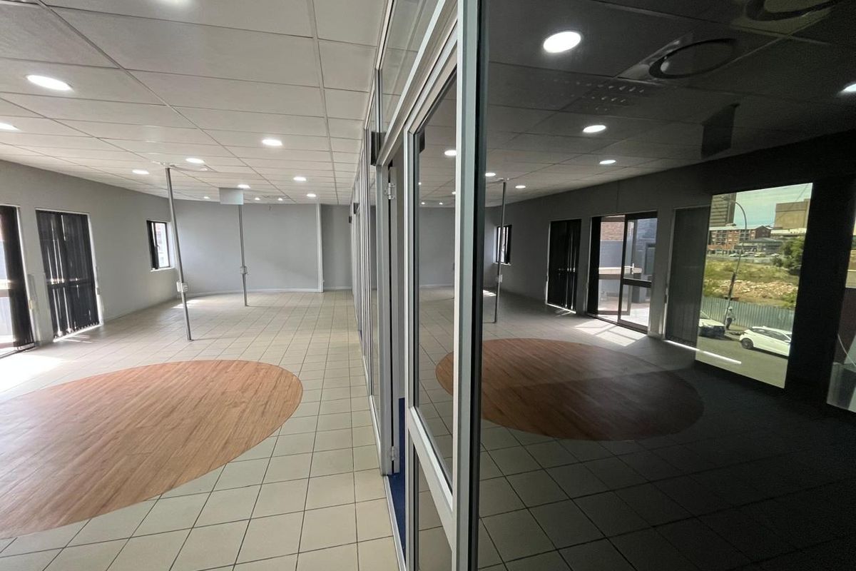 Spacious open-plan office area featuring a modern suspended ceiling, recessed lighting, and a combination of ceramic tile and wood-look flooring with glass partitioning.