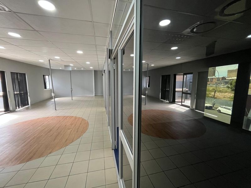 Spacious open-plan office area featuring a modern suspended ceiling, recessed lighting, and a combination of ceramic tile and wood-look flooring with glass partitioning.