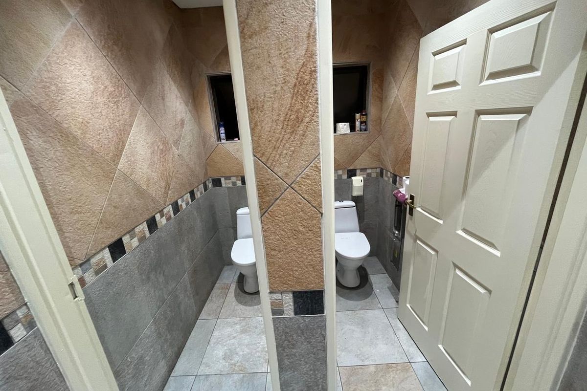 A functional office bathroom featuring dual toilet stalls with tiled walls and flooring, providing a clean and practical layout for staff or visitors.