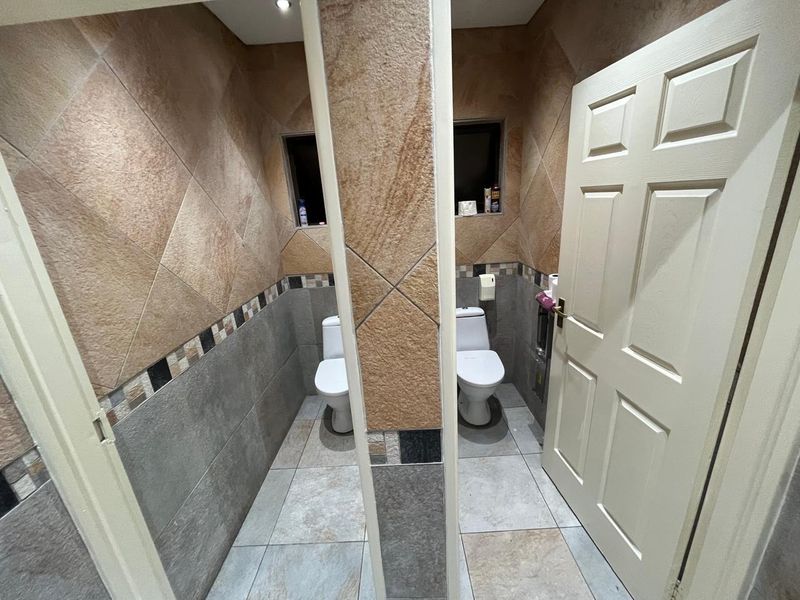 A functional office bathroom featuring dual toilet stalls with tiled walls and flooring, providing a clean and practical layout for staff or visitors.