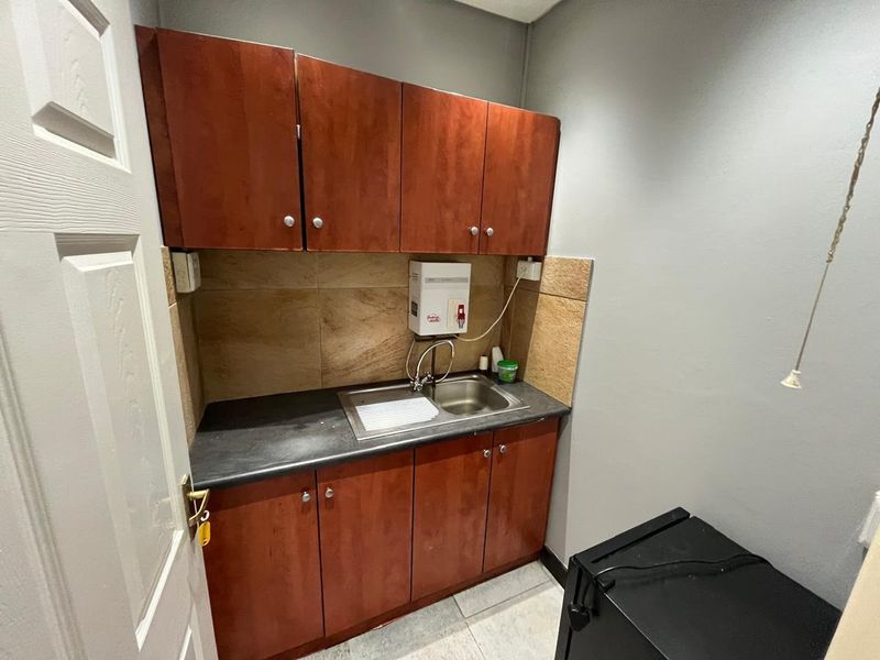 A compact scullery or kitchenette area featuring built-in wooden cabinetry, a stainless steel sink, and a tiled backsplash.