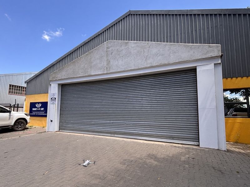 Industrial warehouse exterior featuring a large roller shutter door, corrugated metal siding, and paved driveway access.