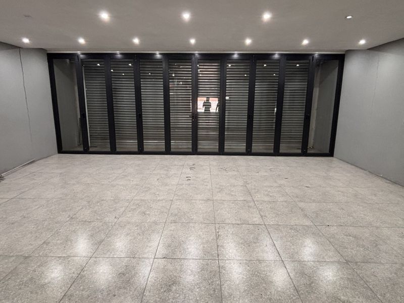 Spacious, modern open-plan area featuring large format floor tiles, recessed downlighting, and expansive black aluminium stacker doors leading to the exterior.