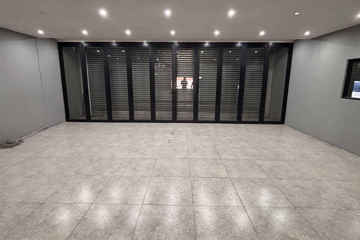 Spacious, modern open-plan area featuring large format floor tiles, recessed downlighting, and expansive black aluminium stacker doors leading to the exterior.