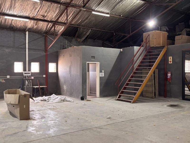 Spacious industrial utility area featuring exposed steel roof trusses, concrete flooring, and a metal staircase leading to an upper mezzanine level.