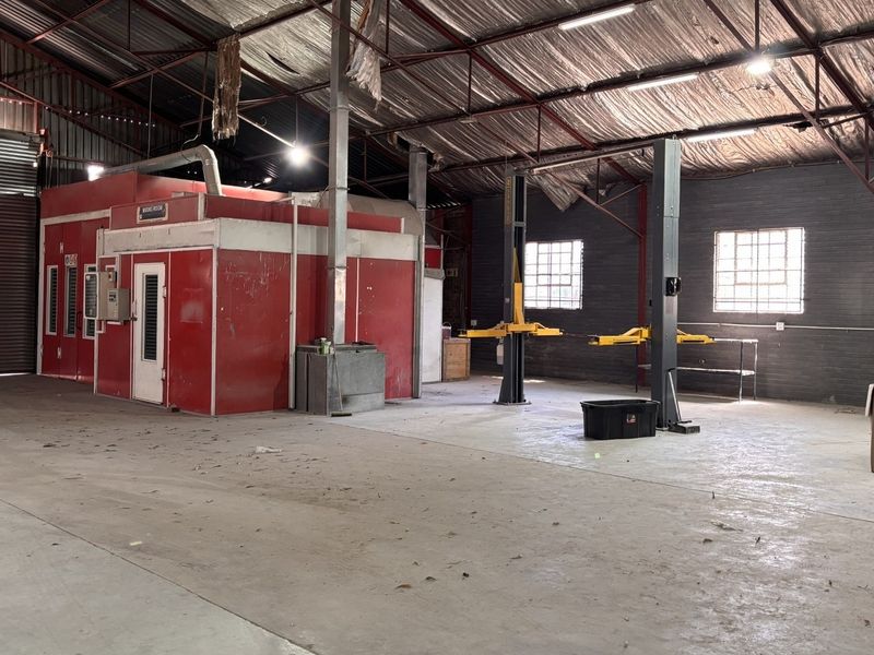 Spacious industrial workshop featuring a built-in spray booth, vehicle hoist, high-clearance roller shutter door, and exposed steel roof structure.