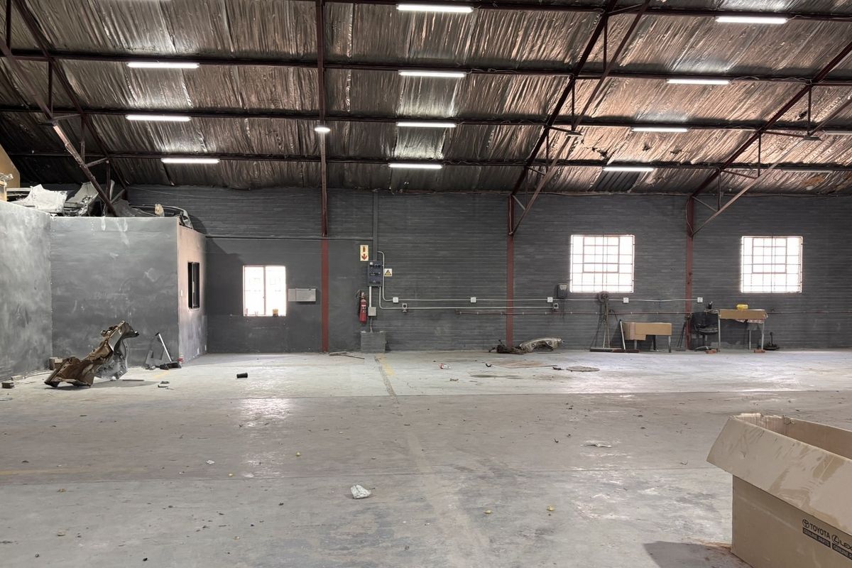 Spacious industrial warehouse featuring high ceilings with exposed steel trusses, concrete flooring, and functional lighting, suitable for various commercial or storage applications.