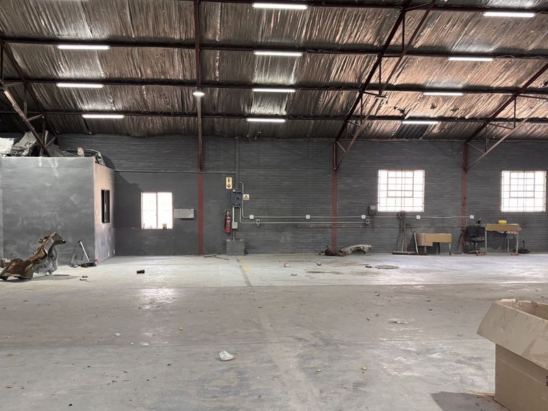 Spacious industrial warehouse featuring high ceilings with exposed steel trusses, concrete flooring, and functional lighting, suitable for various commercial or storage applications.