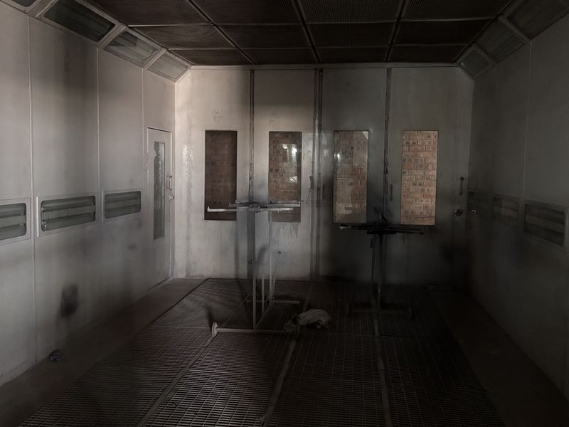 Industrial spray booth featuring metal floor grating, integrated lighting, and ventilation panels, suitable for automotive or industrial finishing applications.