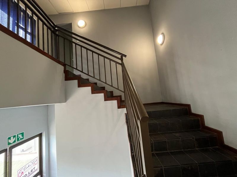 A functional interior stairwell featuring tiled steps, a metal balustrade, and wall-mounted lighting, providing access between levels in a commercial building.