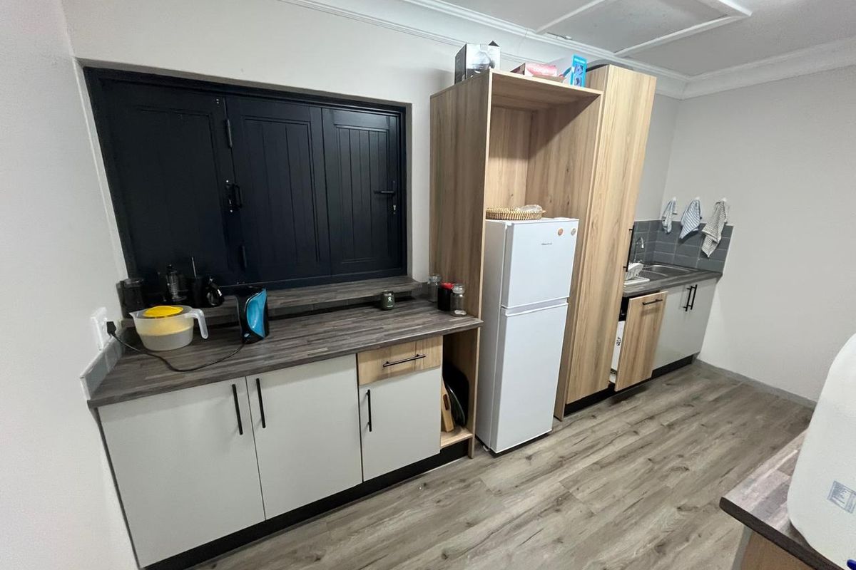 A functional kitchenette featuring modern laminate cabinetry, wood-look vinyl flooring, a stainless steel sink, and a tiled backsplash.