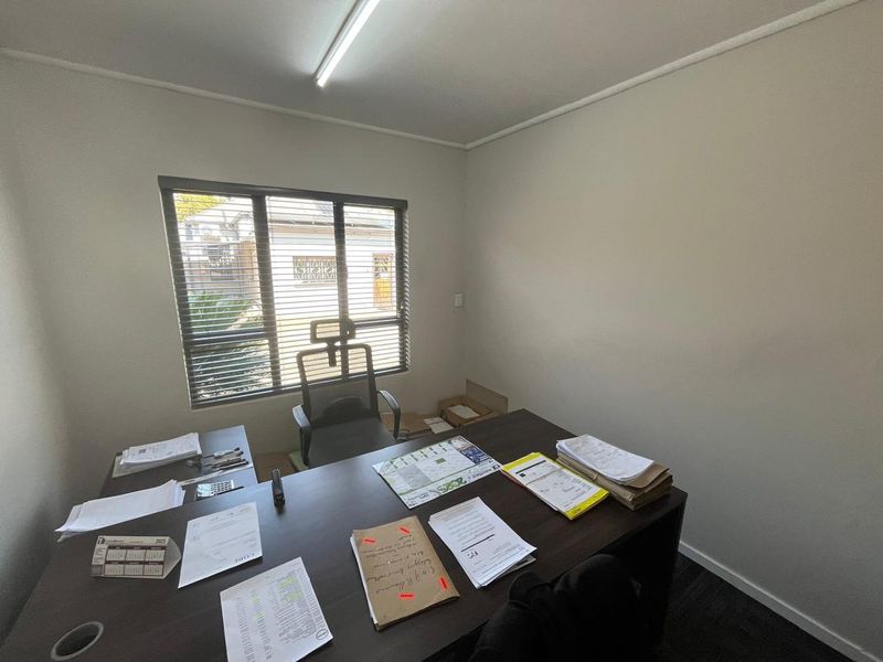 A functional office space featuring neutral walls, a large window with venetian blinds, and a standard fluorescent light fixture.