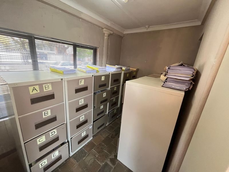 A functional office space featuring stone tile flooring, horizontal window blinds, and coved ceilings, currently utilized for document storage.