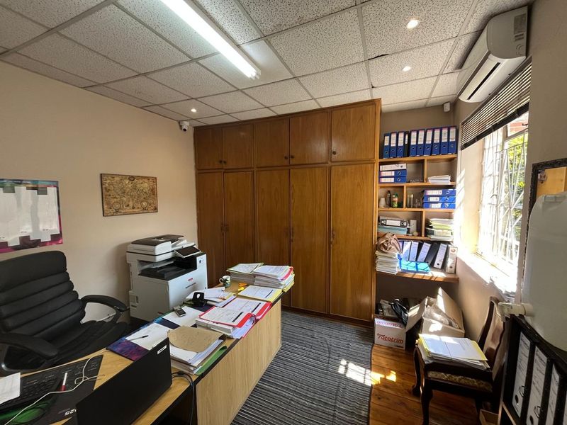 A functional office space featuring extensive built-in wooden cabinetry, integrated shelving, a suspended ceiling, and a split-system air conditioner.