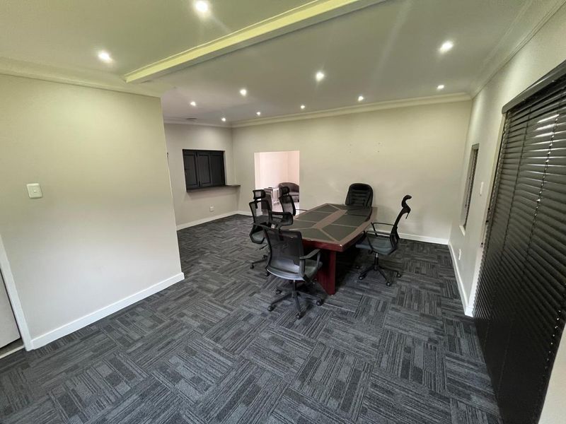 A professional office space featuring modern carpet tiles, recessed downlighting, and a convenient serving hatch, suitable for a meeting or workspace.