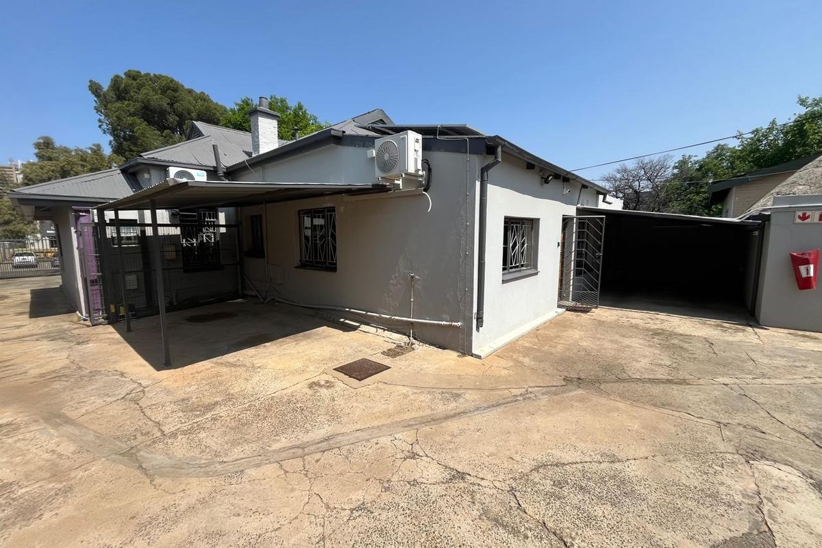 Rear exterior view of the office property featuring a concrete driveway, metal carport, and security bars on windows.