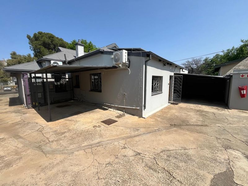 Rear exterior view of the office property featuring a concrete driveway, metal carport, and security bars on windows.