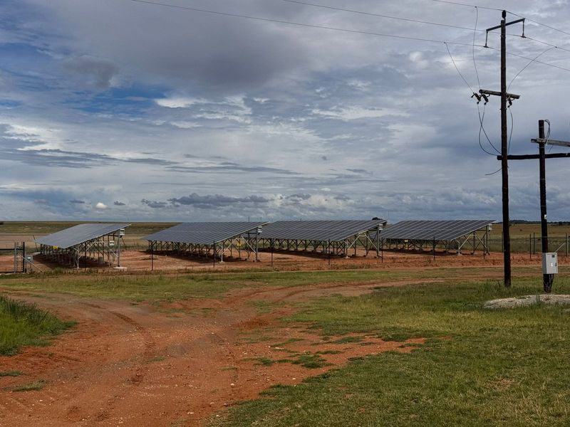 A ground-mounted solar panel array installation situated on a rural farm property, featuring metal support structures and associated electrical infrastructure.