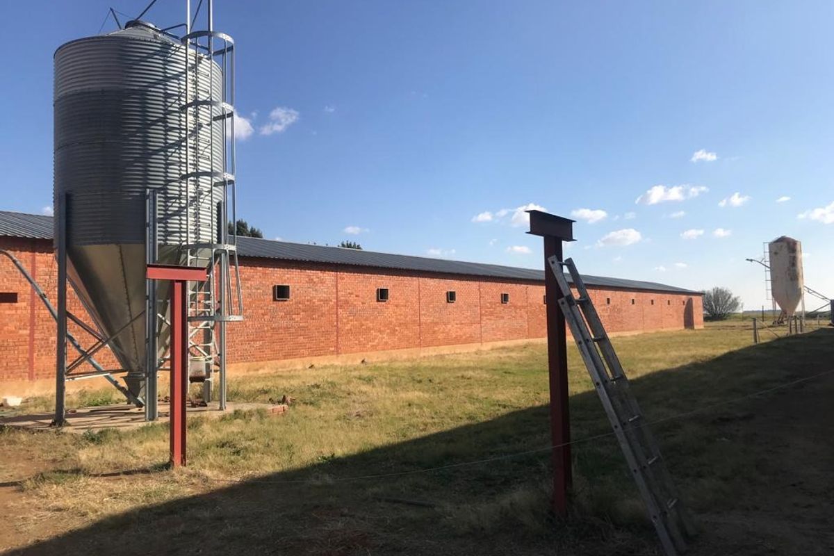 Exterior view of a farm property featuring a large brick barn, metal grain silo, and steel structural supports on the grounds.