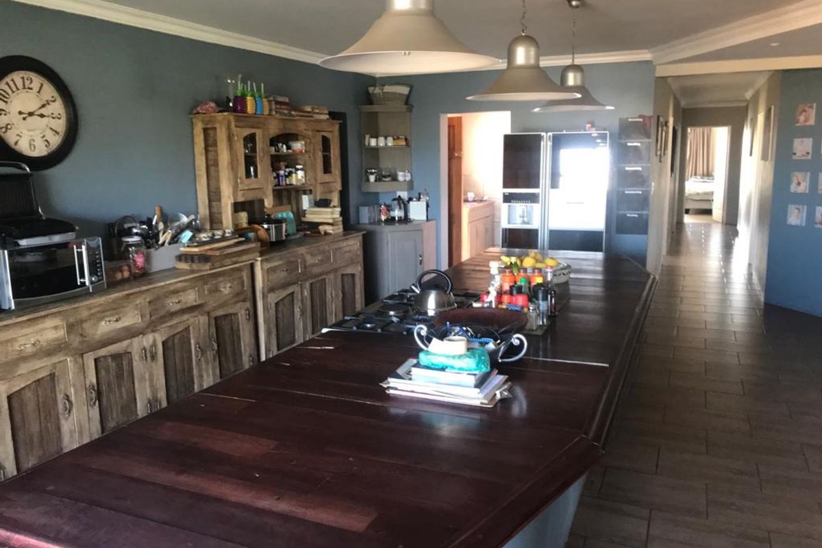 Spacious kitchen featuring a large wooden island with integrated gas hob, ample built-in cabinetry, and tiled flooring, leading into a hallway.