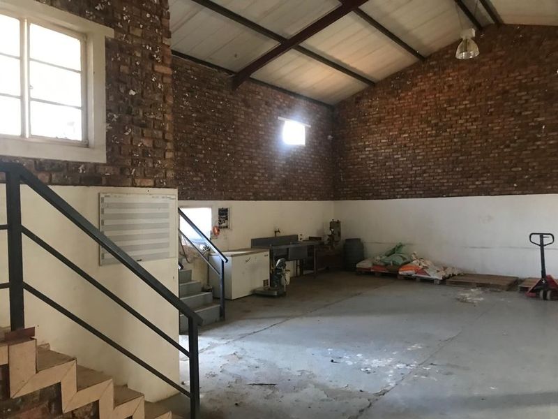 Spacious industrial utility area featuring exposed brick walls, concrete flooring, and a metal staircase, suitable for workshop or storage use.