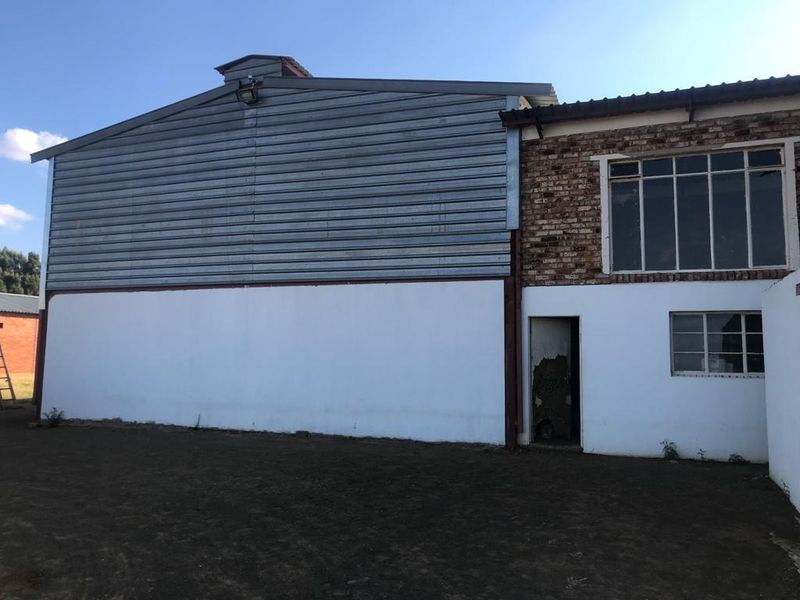 Rear view of a farm building featuring a combination of corrugated metal cladding and exposed brickwork with steel-framed windows.