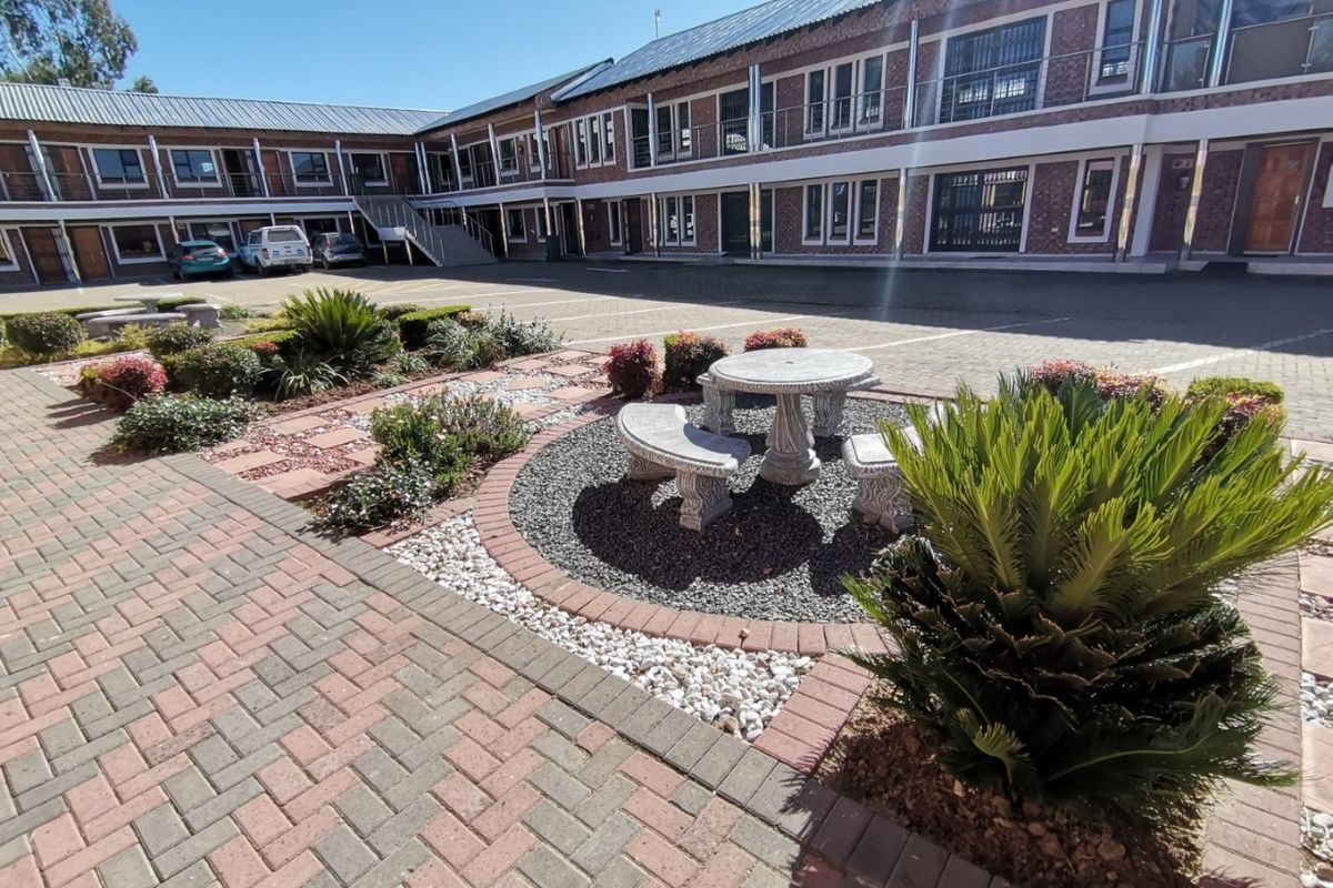 A well-maintained exterior courtyard featuring paved surfaces, brick building facades with balconies, and landscaped garden areas with stone seating.